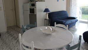 Een knus leefruimte met een eettafel, stoelen, een blauwe bank en een keuken met koelkast en magnetron.