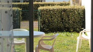 Een kamer met een schuifglasdeur die uitkomt op een terras met twee plastic stoelen en een tafel.