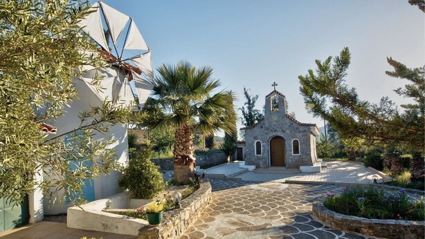 A stone pathway leading to a small church with a bell tower, surrounded by olive trees and potted plants. - Villa AnnaMaria (Minoa Pediada)