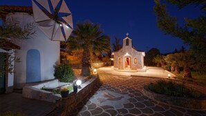 A stone pathway leading to a small church with a bell tower, surrounded by palm trees and illuminated by warm lighting. - Villa AnnaMaria (Minoa Pediada)