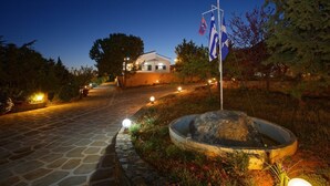 A stone pathway leading to a house with a flagpole and a flag. - Villa AnnaMaria (Minoa Pediada)
