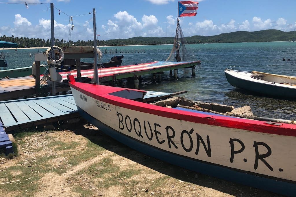 Un bote llamado BOQUERON P.R. atracado en un muelle con un flotador salvavidas y una pequeña bandera.