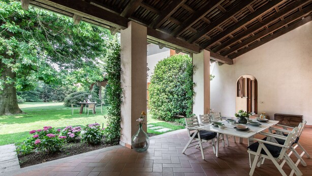 An outdoor patio with a table and chairs, surrounded by greenery and a view of a garden. - Beautiful villa with pool surrounded by nature near Golf and Tennis courts (Beregazzo con Figliaro (Co))
