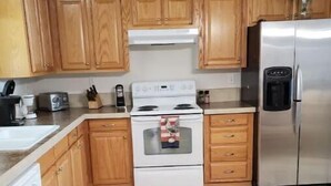 Une cuisine avec des meubles de rangement en bois, un fourneau blanc, un réfrigérateur en acier inoxydable et un sol carrelé.