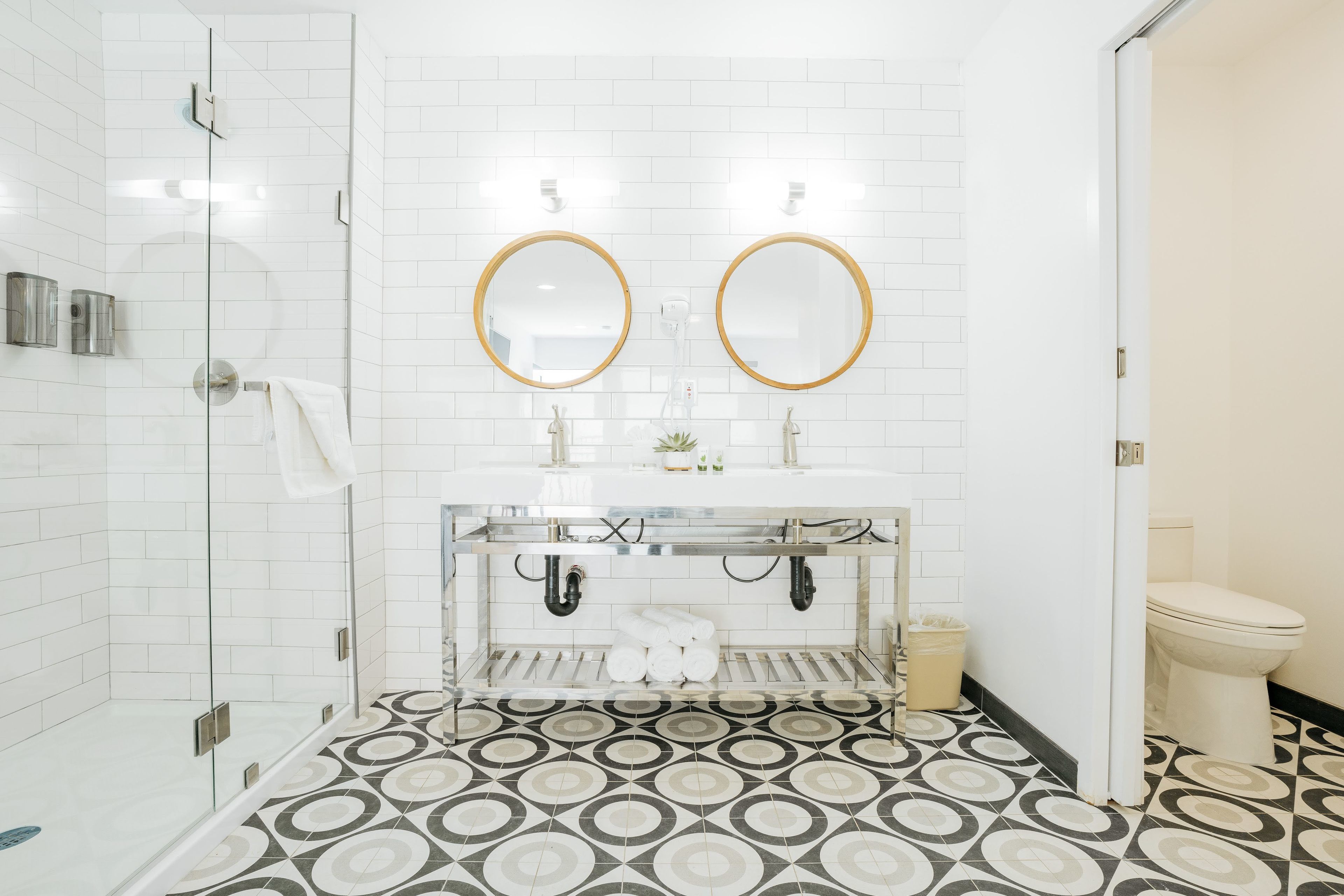 A bathroom with a shower, two sinks with mirrors, a toilet, and patterned floor tiles.