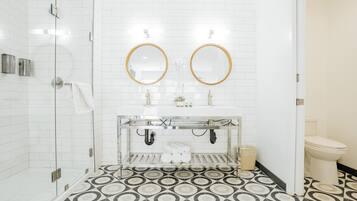A bathroom with a shower, two sinks with mirrors, a toilet, and patterned floor tiles.