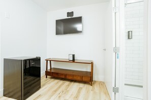 A room with a built-in wooden bench, a wall-mounted flat-screen TV, and a built-in stainless steel refrigerator. - The Belmont Shore Inn (Long Beach)