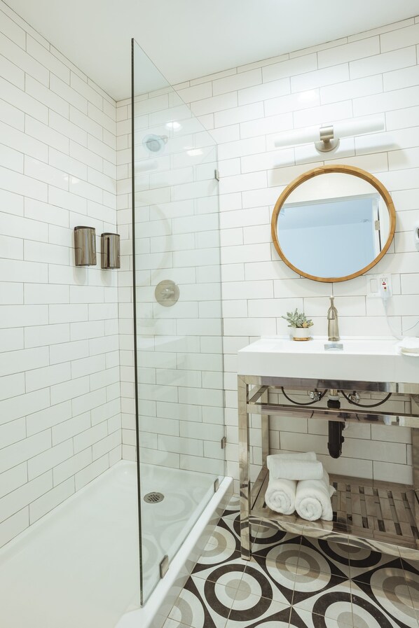 A modern bathroom with white subway tiles, a glass-enclosed shower, a round mirror, and a white sink with a small plant.