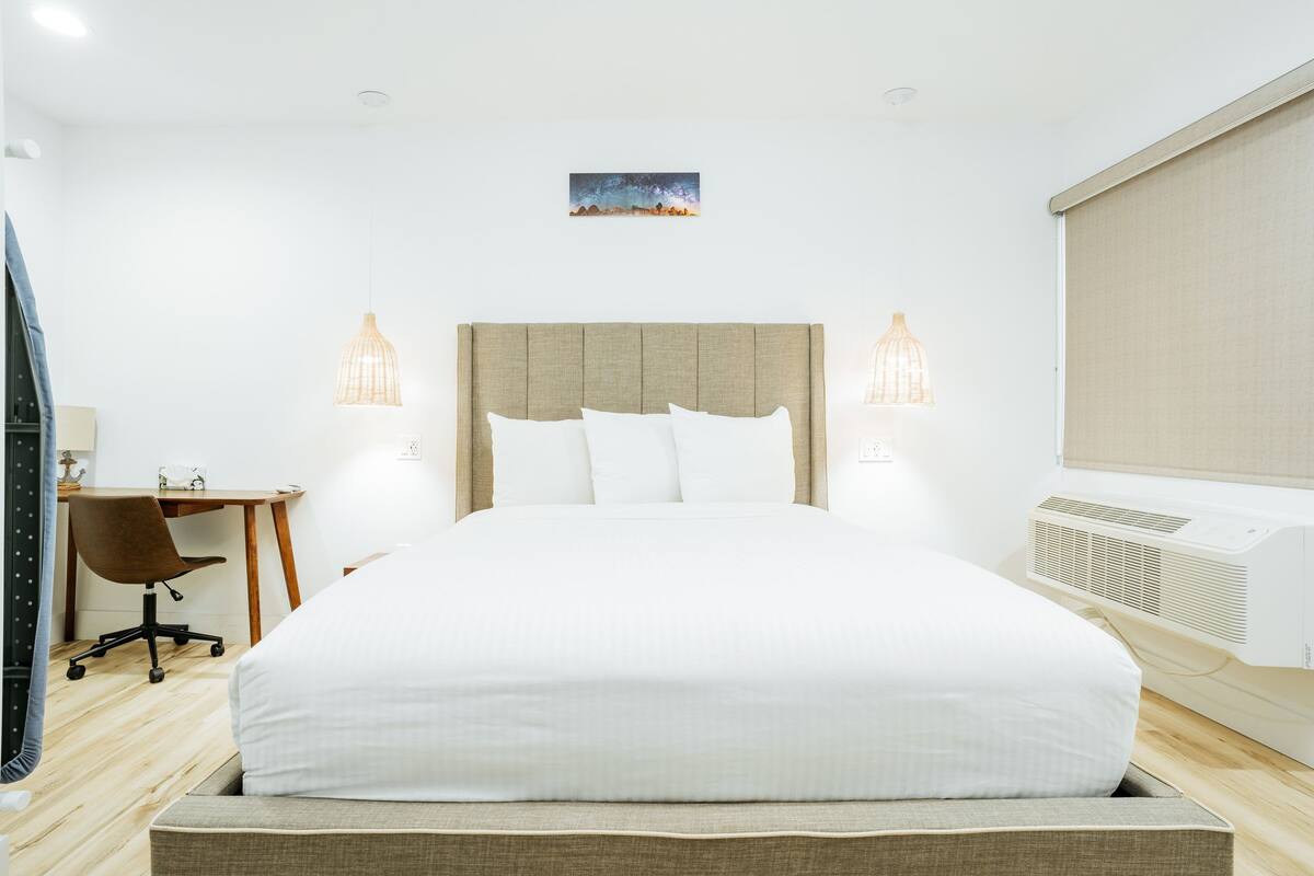 A hotel room with a large bed, two bedside lamps, a desk with a chair, and a small painting on the wall.