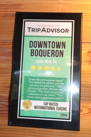 Kehyksiin asetettu TripAdvisor-arvostelu, joka koskee Cabo Rojon kaupungin keskustan Boqueron-aluetta, Puerto Rico, ja jossa korostetaan asiakkaiden antamia arvioita sekä vuonna 2019 myönnettyä palkintoa parhaana kansainvälisenä ravintolana.
