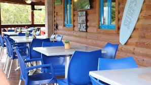 Una cabaña de madera con sillas y mesas azules, un letrero con forma de tabla de surf y un letrero que dice 'Este es mi lugar feliz'.