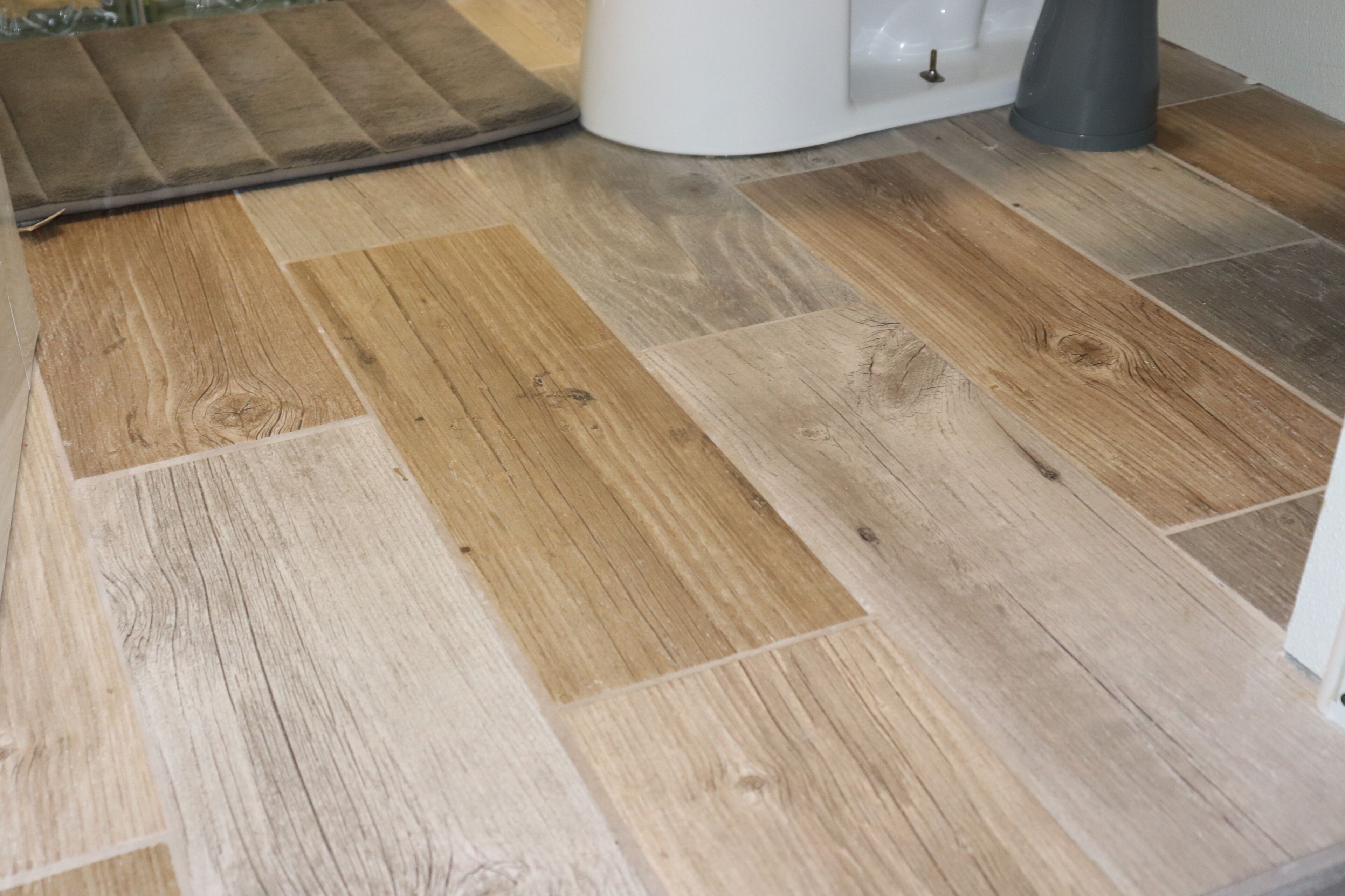 Un piso de madera con un felpudo y un objeto blanco, posiblemente un cubo de basura, en una habitación.