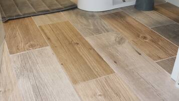 Un piso de madera con un felpudo y un objeto blanco, posiblemente un cubo de basura, en una habitación.