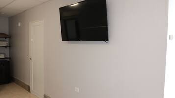 A room with a flat-screen TV mounted on the wall, a white door, and a tiled floor.