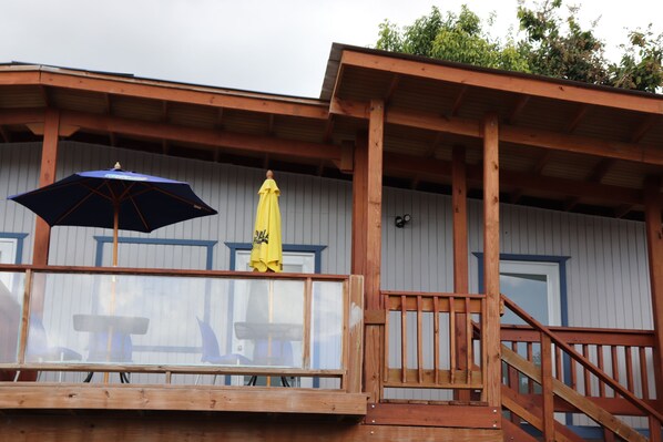 A wooden deck with a glass railing, a yellow umbrella, and a blue umbrella.
