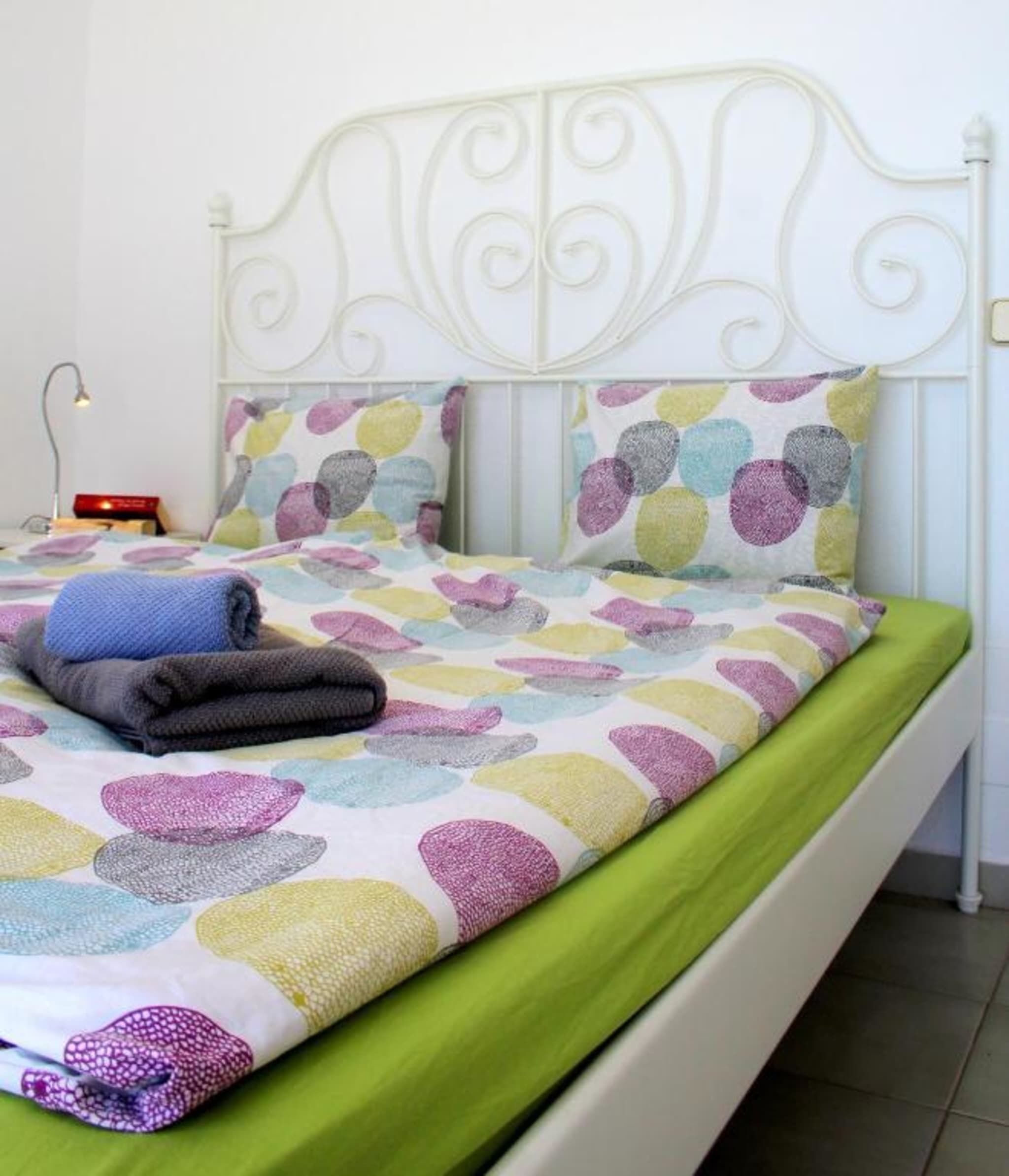 A bed with a white metal headboard, a colorful bedspread with circular patterns, and a green bed skirt.