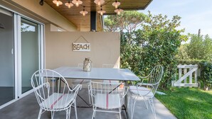 An outdoor patio with a white table and chairs, a hanging light fixture, and a 'BEACH' sign on the wall.