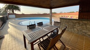 A covered outdoor area with a pool, a table with chairs, and a stone wall. - Finca Canal, Rural Villa in the Comarca de la Sidra (Quintueles)