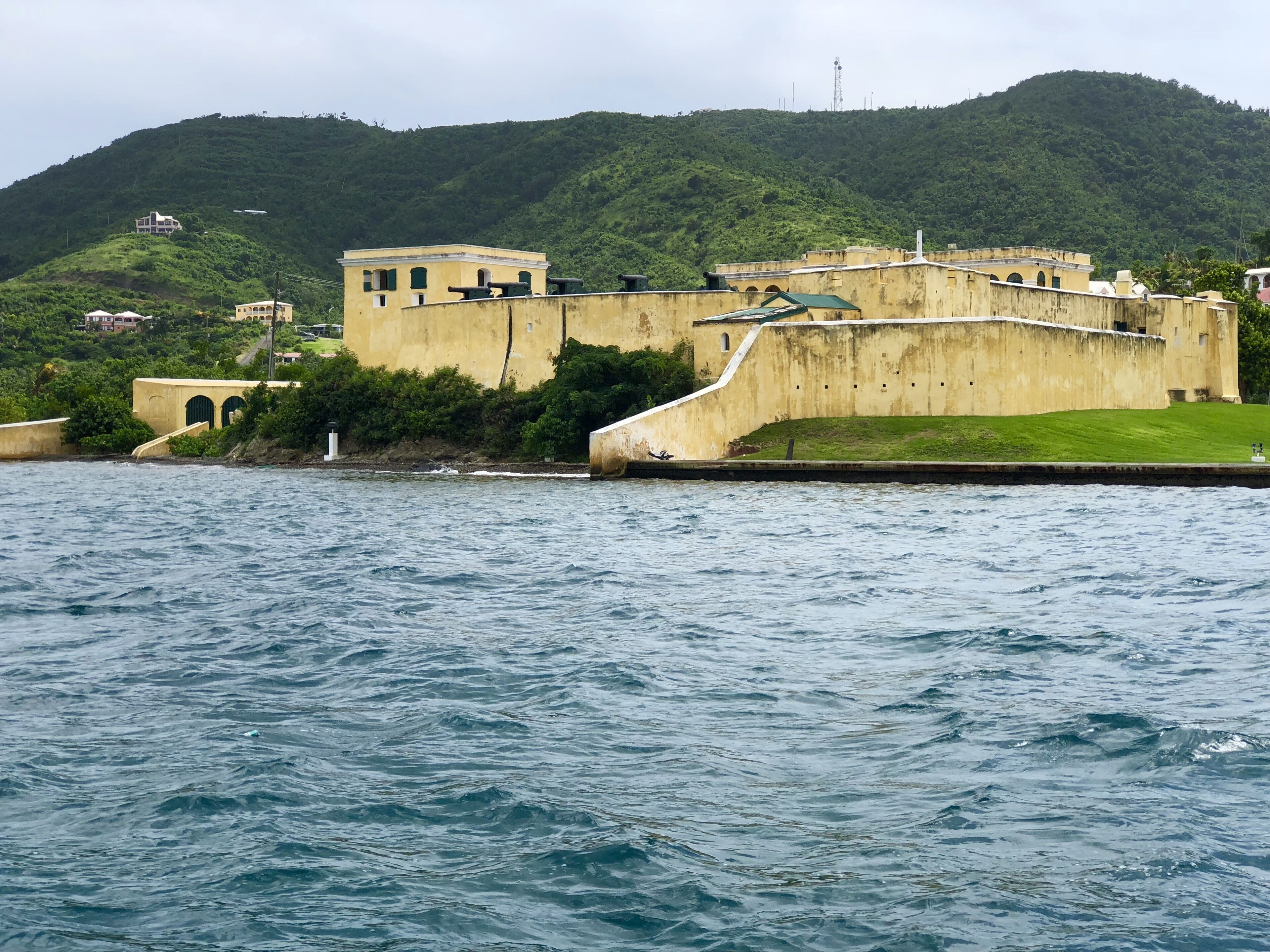 A coastal fort with a large water body in the foreground and a hill with vegetation in the background.