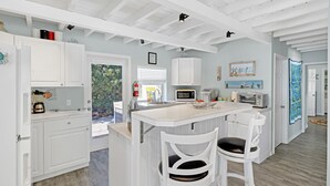 Une cuisine moderne avec des meubles blancs, un îlot central doté de tabourets de bar et une vue sur l’extérieur.
