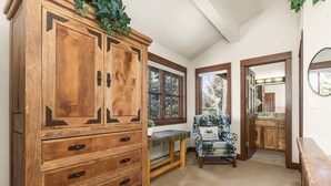 A wooden cabinet with drawers, a bench, and a chair with a cushion in a room with a window and a mirror.