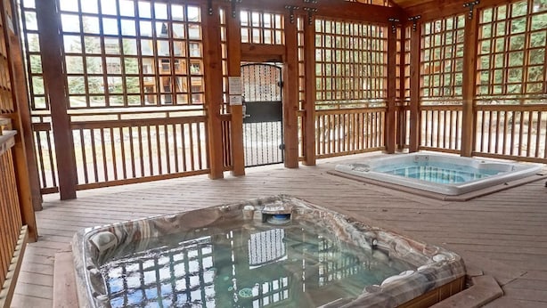 A wooden deck with two hot tubs and a covered area with a view of a cabin.