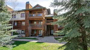 A multi-story log cabin with a balcony, a stone foundation, and a well-maintained lawn.