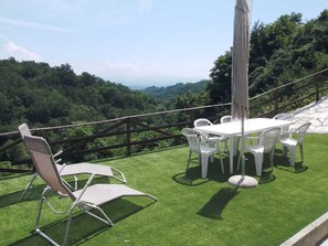 Eine Terrasse mit weißem Tisch und Stühlen, umgeben von einem Holzzaun, mit Blick auf eine üppige grüne Landschaft.