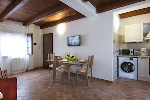 A compact kitchen with a washing machine, a dining table with chairs, and a television mounted on the wall.