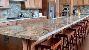 A kitchen with wooden cabinets, a stainless steel refrigerator, a granite countertop, and bar stools. - The EDGE:  Picturesque & Secluded Gem - Scenic View (Shaver Lake)