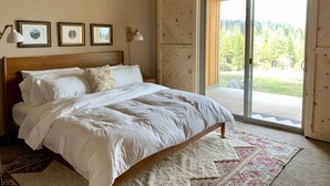 A bedroom with a large bed, framed pictures on the wall, and a view of a forest through a sliding glass door. - The EDGE:  Picturesque & Secluded Gem - Scenic View (Shaver Lake)
