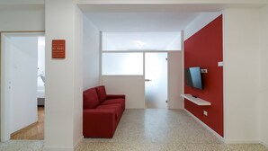 En moderne stue med en rød sofa, et fjernsyn på en hvid reol og et stort vindue.
