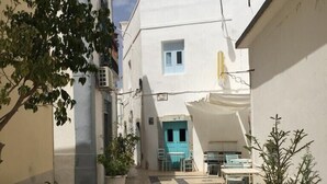 A narrow cobblestone alleyway between buildings with a blue door and outdoor seating area.