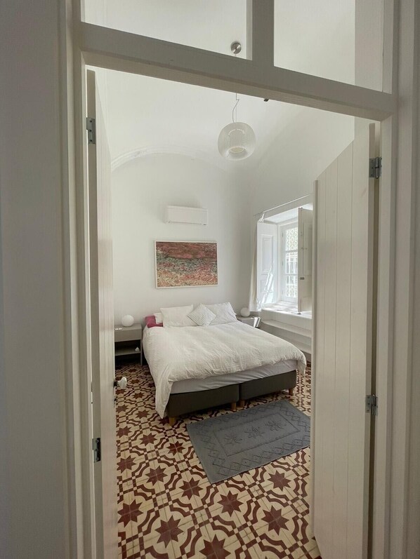 A bedroom with a bed, a window, a radiator, and a patterned floor. - Renovated, authentic fisherman's house in the historic city center CO2 neutral (Olhão)