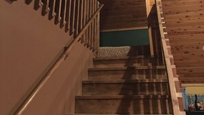 A wooden staircase with a handrail, leading to a landing with a green wall and a small window.