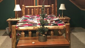 A cozy attic bedroom with a wooden bed, two bedside lamps, a quilt, and a small potted plant.