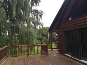 Une terrasse en bois avec une rambarde, un espace couvert avec un toit et une grande fenêtre.
