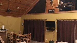 A cozy loft-style room with a wooden ceiling, a dining area with a wooden table and chairs, a sofa, and a ceiling fan.