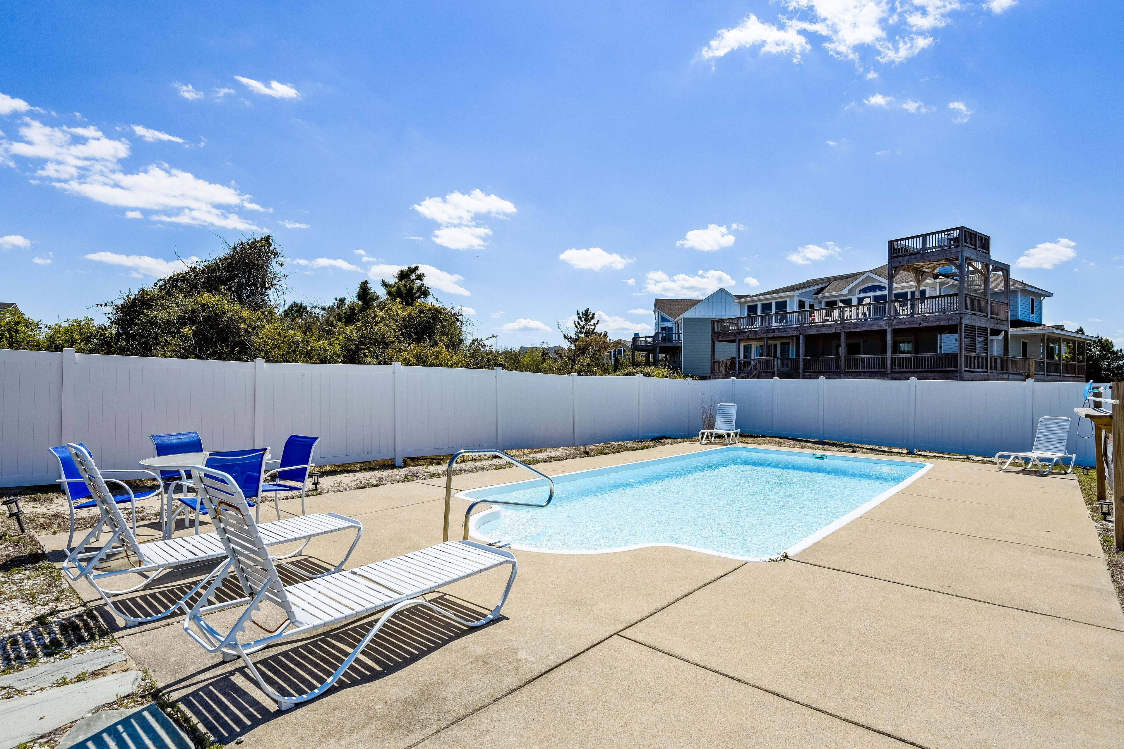 A backyard with a swimming pool, lounge chairs, and a two-story house.