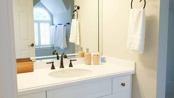 A bathroom with a white vanity, two sinks, a large mirror, and a towel rack.