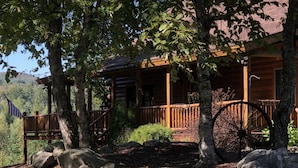 A log cabin with a porch, large rocks, and a wooden wheel.
