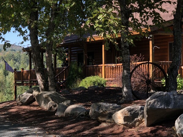 A log cabin with a porch, large rocks, and a wooden wheel.
