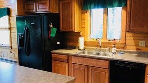 A kitchen with wooden cabinets, a black refrigerator, a sink, and a dishwasher.
