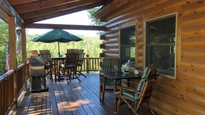 A wooden deck with outdoor seating, a grill, and a table with drinks.