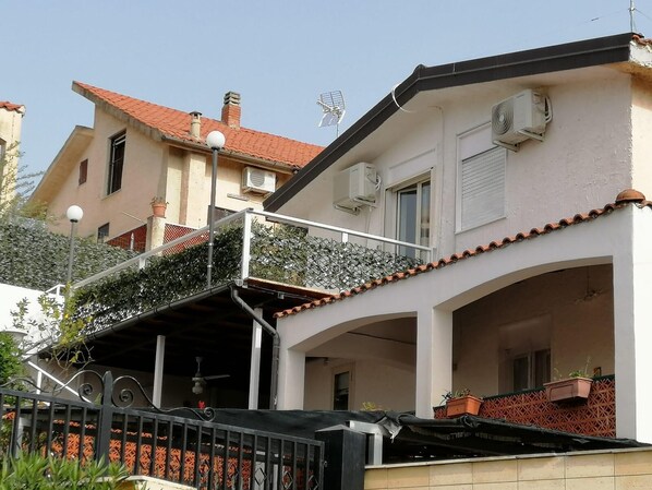 Un edificio de dos pisos con balcón, unidades de aire acondicionado y techo de tejas.