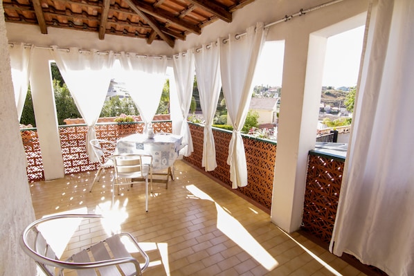 A sunlit balcony with a table and chairs, a view of the city, and a wooden ceiling. - Seaside cottage in residence (Costa Saracena)