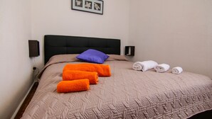 A neatly made bed with a beige quilt, a purple pillow, and several rolled towels. - Seaside cottage in residence (Costa Saracena)