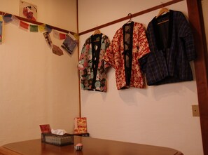 A room with a wooden table, a hanging clothes rack with various garments, and a wall with a few items.