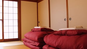 Une pièce de style japonais traditionnel, avec un sol recouvert de tatamis, une porte coulissante en papier de riz (shoji) et une pile de futons rouges.