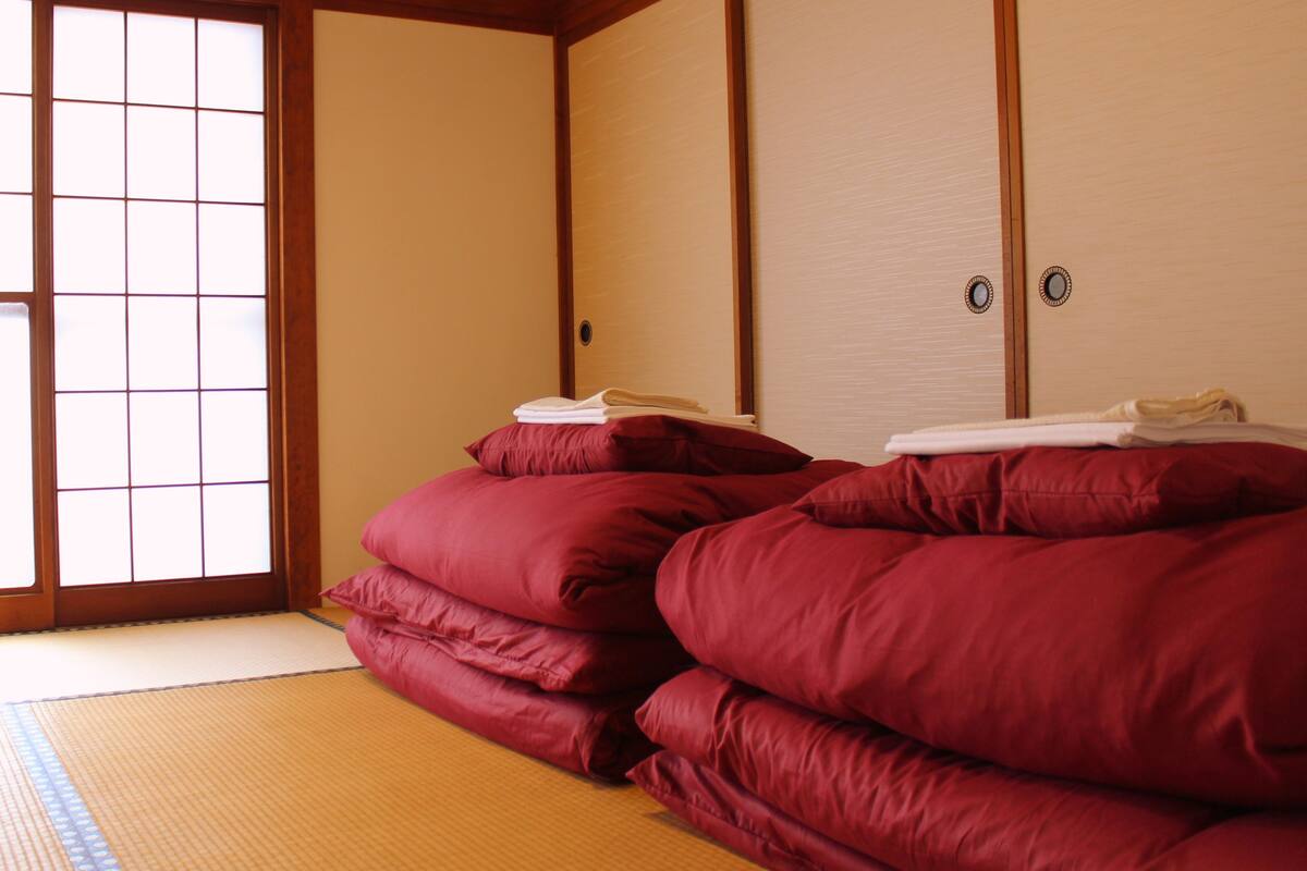 Una habitación tradicional japonesa con suelo de tatami, puerta corrediza de shoji y un montón de colchones futón rojos.